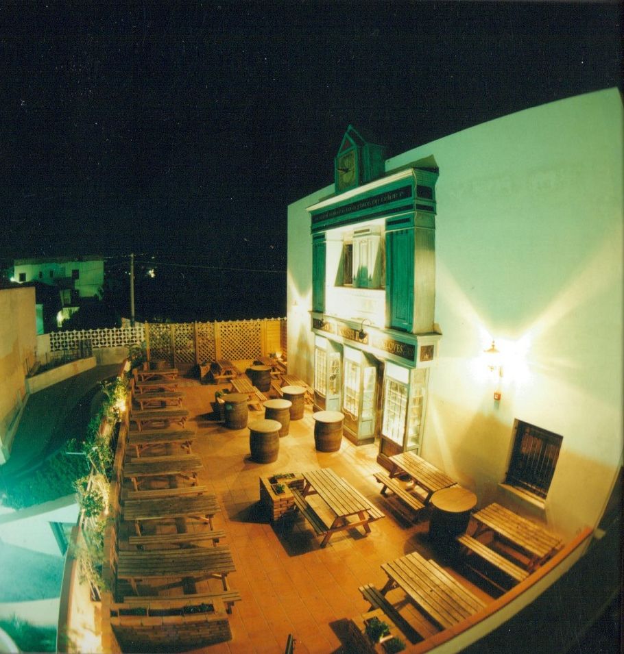 La terrazza esterna del Molly's Pub di sera, con tavoli in legno e la facciata verde illuminata.