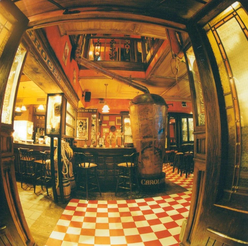 Il bancone del Molly's Pub, con pavimento a scacchi rosso e crema e la botte centrale.